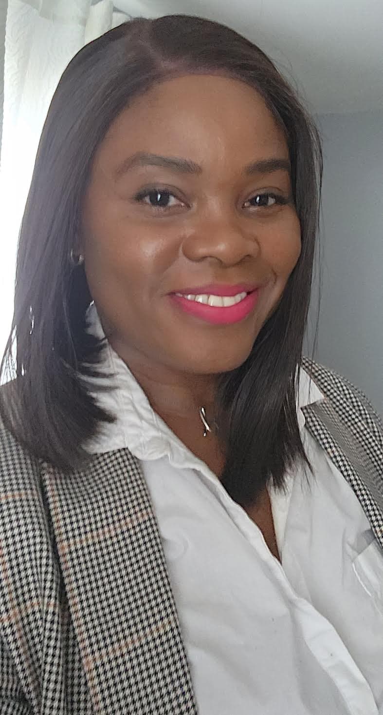 Smiling woman with dark skin, pink lipstick, wearing a white blouse and patterned blazer.